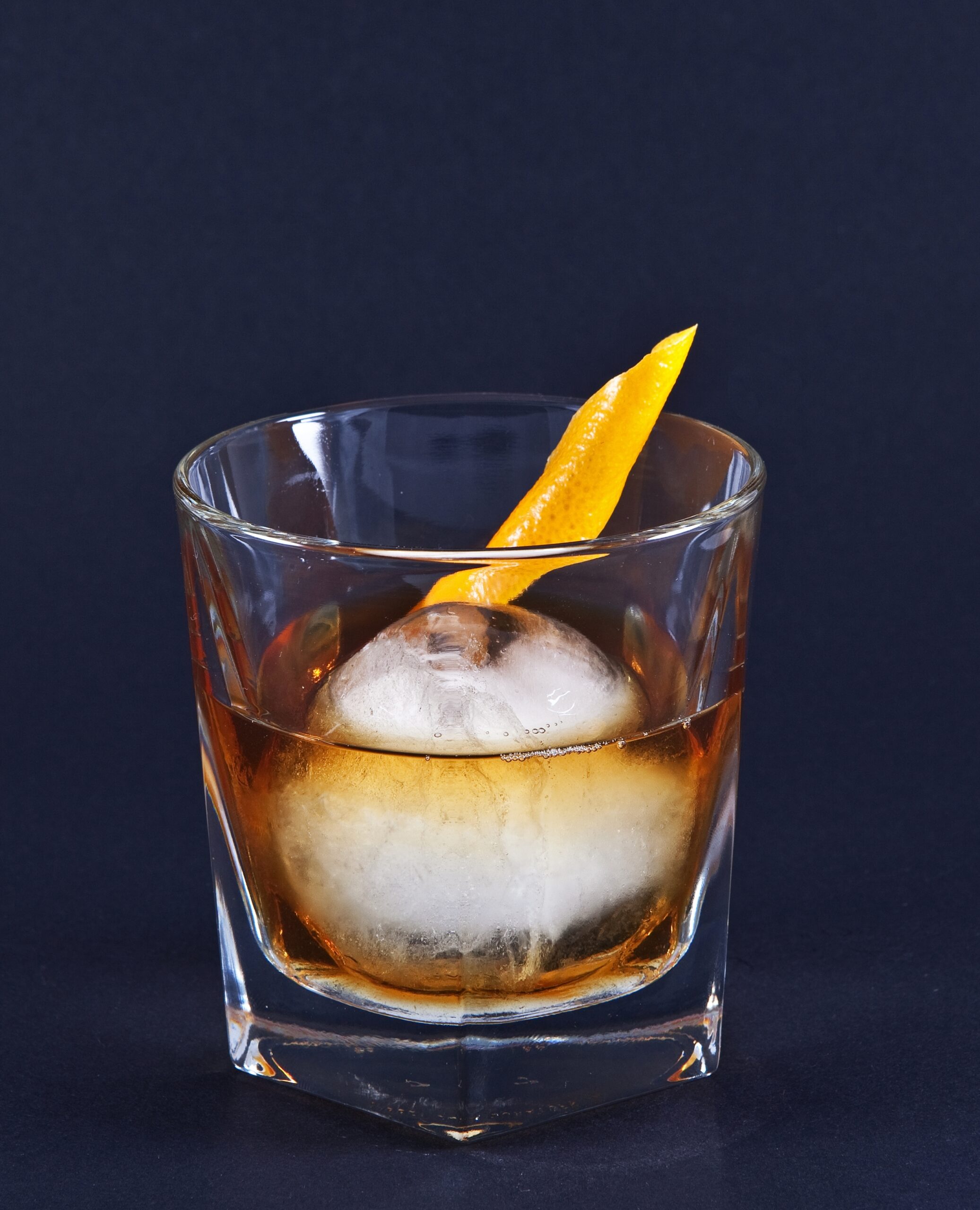 An Old Fashioned over a large ice sphere with an orange twist